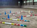 Bunte Stangen und blaue Kegel bilden einen Parcours in einer Reithalle. Der **Abstand der Trabstangen** ist für das Training eines Pferdes vorbereitet.