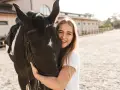 Glückliches Mädchen umarmt ein schwarzes Pferd, eine beliebte Pferderasse mit ruhigem Temperament.