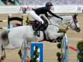 Reiterin und Schimmel springen über Hindernis. Der Aufbau der **Springgymnastik** zeigt die Eleganz und Kraft des Pferdesports.