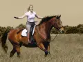 Eine Frau mit blonden Haaren reitet fröhlich auf einem braunen Pferd durch ein Feld. Sie trägt Reithosen und Stiefel. Das Bild vermittelt ein Gefühl von Freiheit und Freude beim Reiten.