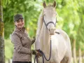 Frau mit Kappe und brauner Jacke streichelt ein helles Pferd. Sie hält eine blaue Leine. Faszientraining Pferd für mehr Wohlbefinden.