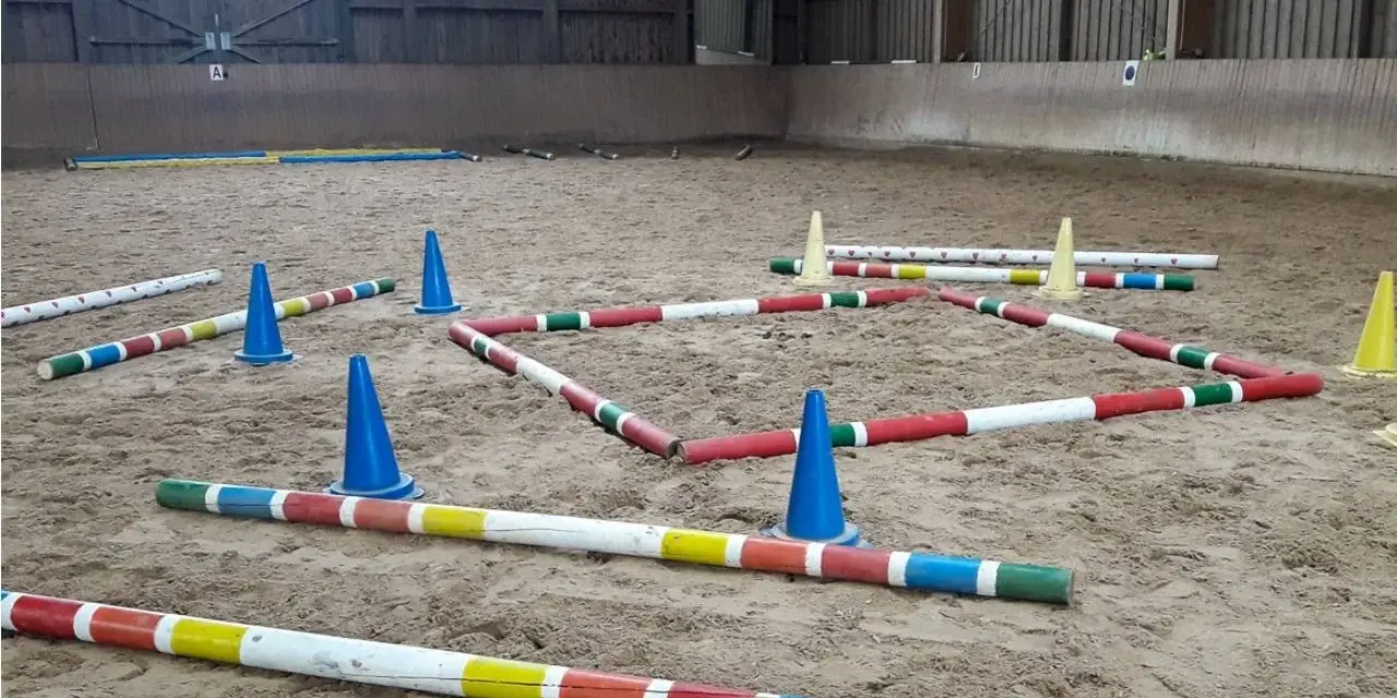 Bunte Stangen und blaue Kegel bilden einen Parcours in einer Reithalle. Der **Abstand der Trabstangen** ist für das Training eines Pferdes vorbereitet.