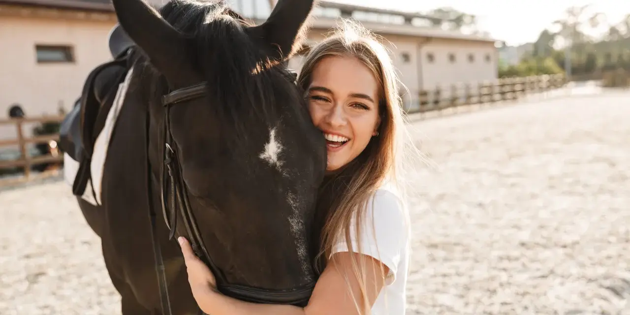 Glückliches Mädchen umarmt ein schwarzes Pferd, eine beliebte Pferderasse mit ruhigem Temperament.