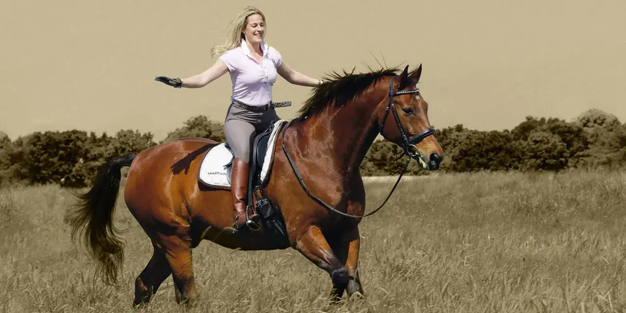 Eine Frau mit blonden Haaren reitet fröhlich auf einem braunen Pferd durch ein Feld. Sie trägt Reithosen und Stiefel. Das Bild vermittelt ein Gefühl von Freiheit und Freude beim Reiten.