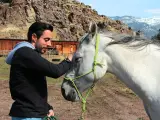 Mann streichelt Pferd, zeigt Vertrauen und Harmonie im **natural horsemanship**. Im Hintergrund eine rustikale Scheune und Berge.