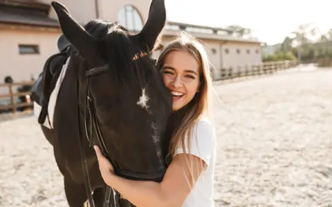 Glückliches Mädchen umarmt ein schwarzes Pferd, eine beliebte Pferderasse mit ruhigem Temperament.