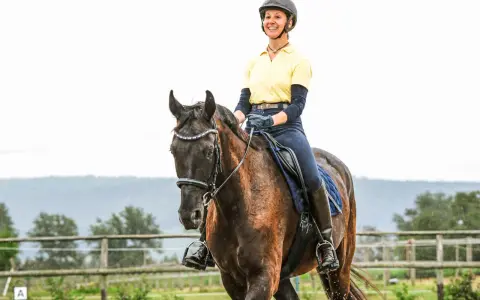Eine Reiterin in gelbem Shirt und Reitstiefeln genießt das Aussitzen beim Reiten auf einem braunen Pferd.