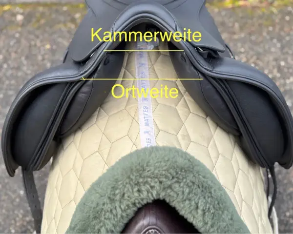 Schwarzer Sattel mit gelben Markierungen für Kammerweite und Ortweite. Ein Maßband liegt darunter.