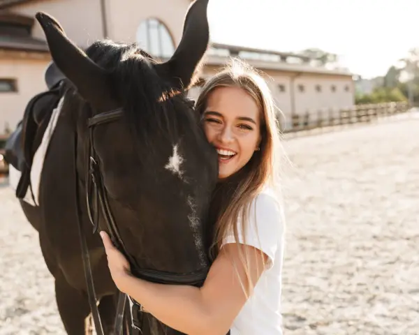 Glückliches Mädchen umarmt ein schwarzes Pferd, eine beliebte Pferderasse mit ruhigem Temperament.