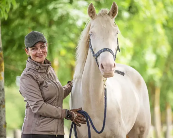 Frau mit Kappe und brauner Jacke streichelt ein helles Pferd. Sie hält eine blaue Leine. Faszientraining Pferd für mehr Wohlbefinden.