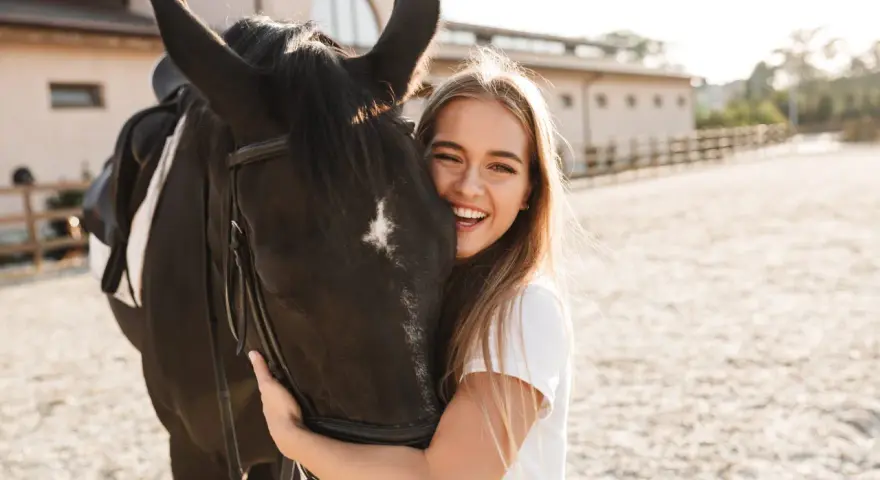 Glückliches Mädchen umarmt ein schwarzes Pferd, eine beliebte Pferderasse mit ruhigem Temperament.