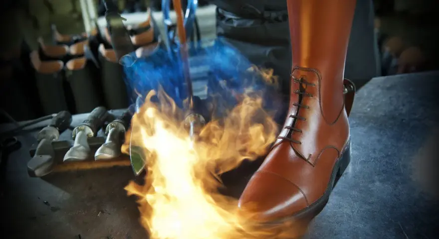 Ein brauner Reitstiefel wird mit einem Brenner bearbeitet. Werkzeuge liegen bereit für die Reitstiefel Pflege.