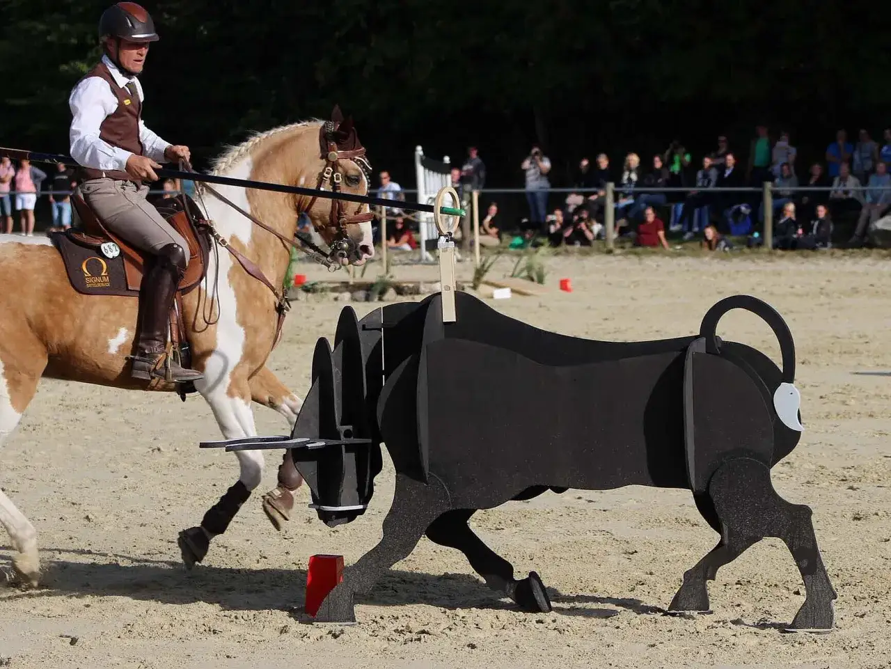 Reiter mit Pferd umrunden einen Stier-Dummy. Das ist ein Hindernis bei Working Equitation, einer Reitsportart.